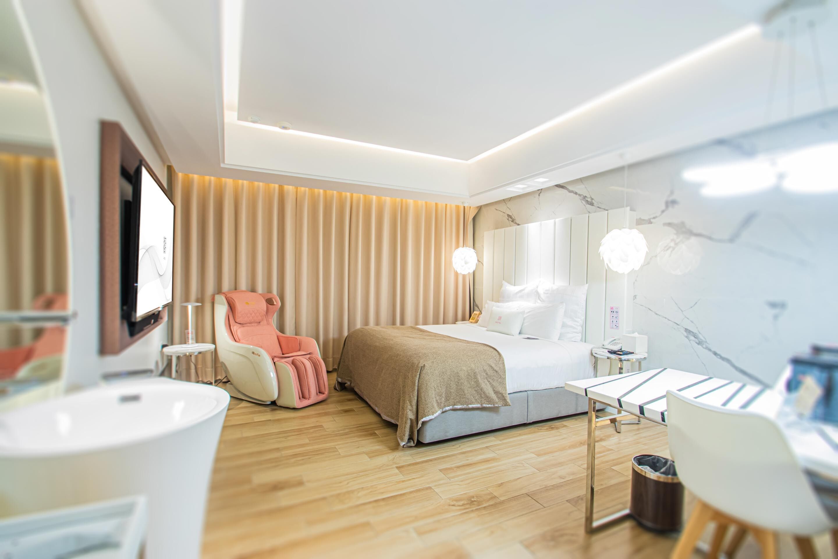 A modern hotel room with a bed, a massage chair, a desk, and a bathroom.