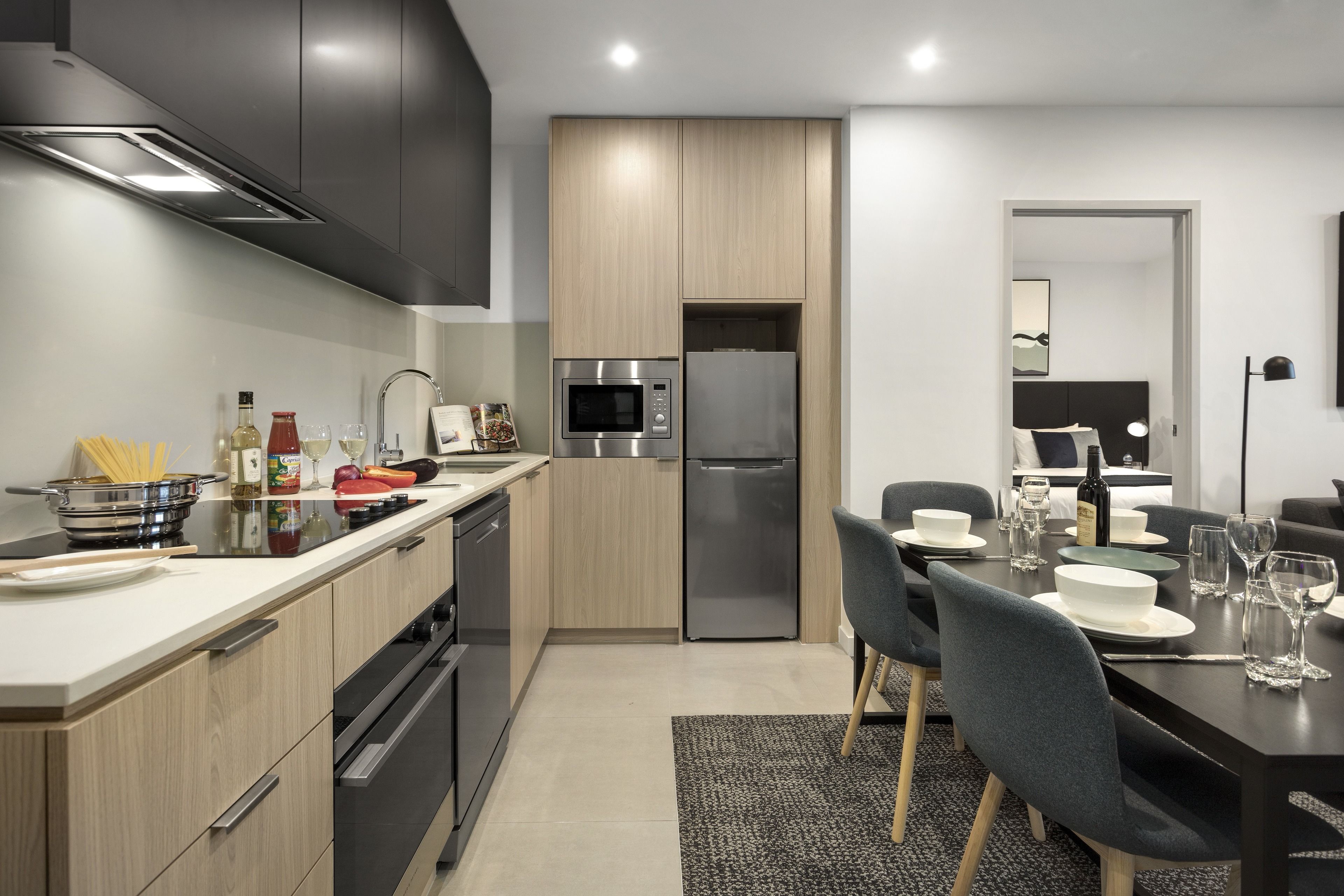 Una cocina moderna con armarios oscuros, un refrigerador de acero inoxidable y un comedor con una mesa dispuesta para cuatro.