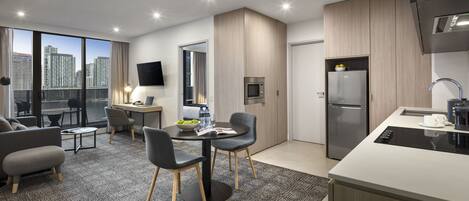 A modern kitchen with a built-in microwave, refrigerator, and sink. There is a dining area with a table and chairs, and a seating area with a sofa and chairs.