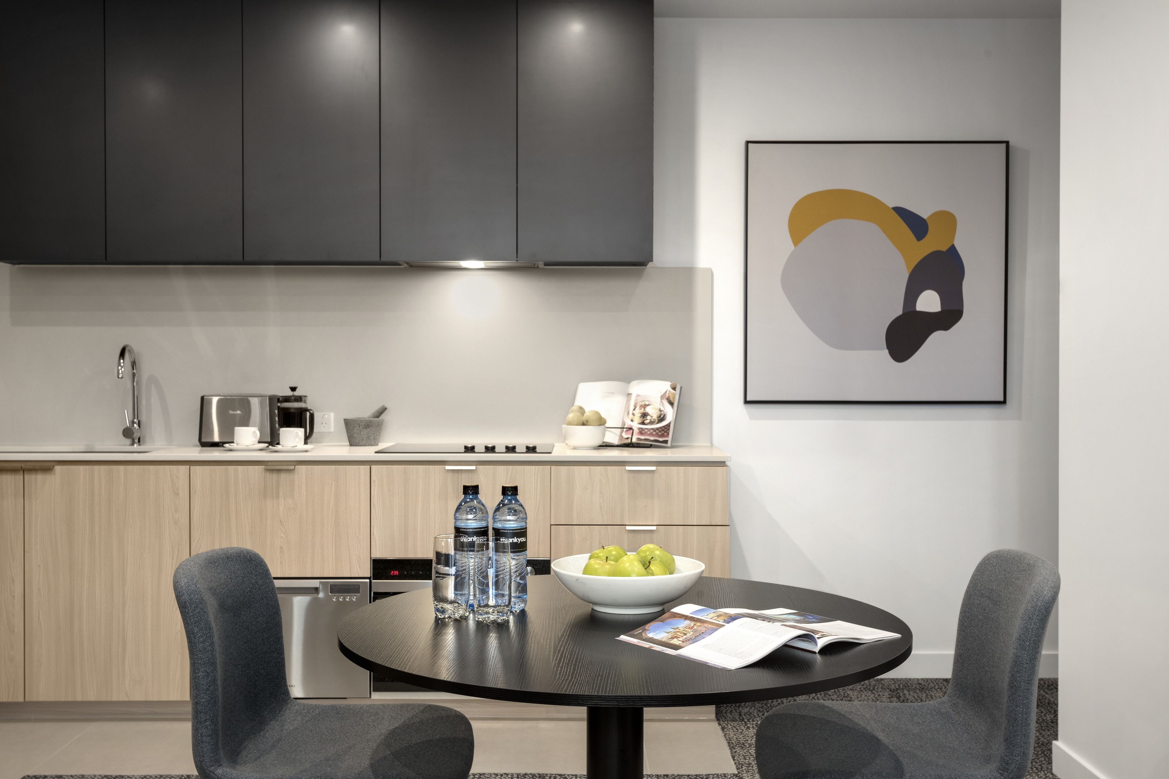 A modern kitchen with dark cabinets, a round dining table, and a bowl of apples.
