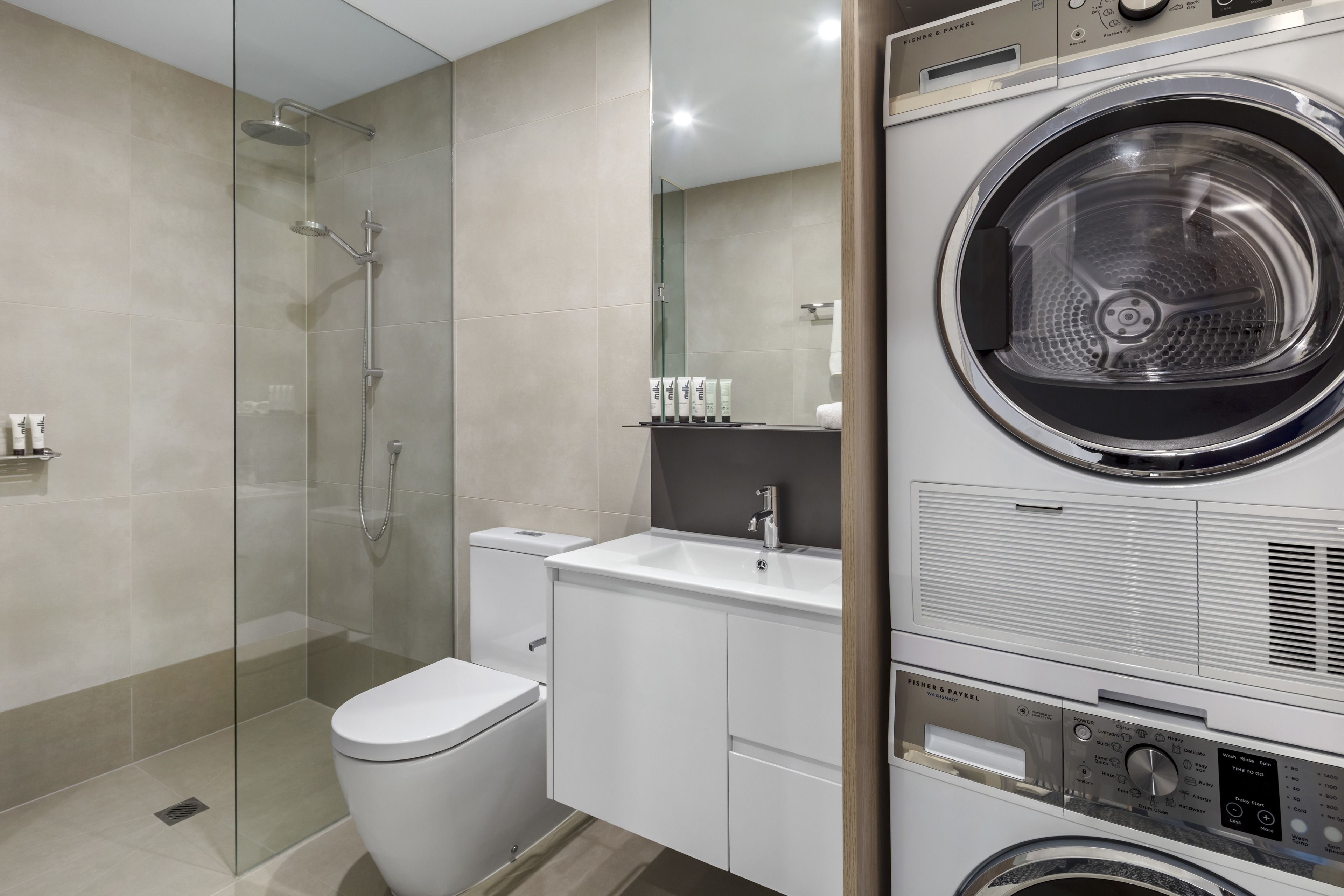 A modern bathroom with a glass-enclosed shower, a white toilet, a sink, and a built-in washer and dryer.