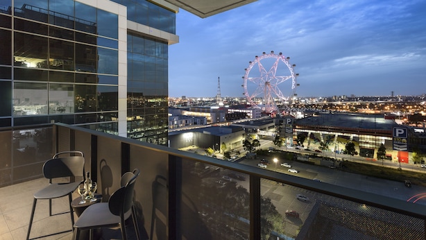 A balcony with two chairs and a table, overlooking a cityscape with a Ferris wheel and a parking area. - Quest NewQuay (Docklands)
