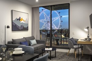 Una habitación de hotel moderna con un ventanal grande, un sofá, una mesa de comedor y un escritorio.