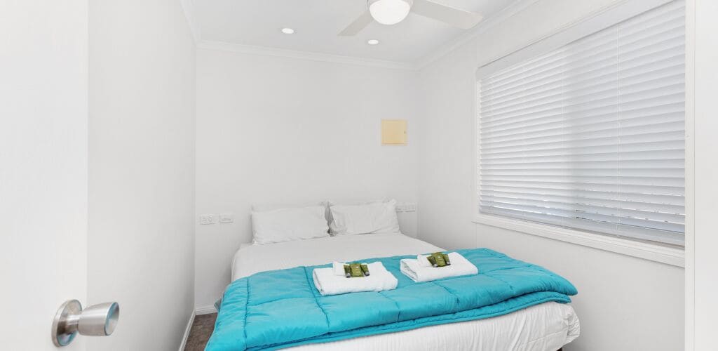 Una habitación de hotel con cama, ventilador de techo, ventana con persianas y puerta con manija.