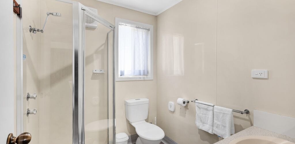 A bathroom with a glass shower enclosure, a toilet, and a sink with a towel rack.