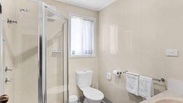 Un baño con cabina de ducha de vidrio, inodoro y lavamanos con barra para toallas.