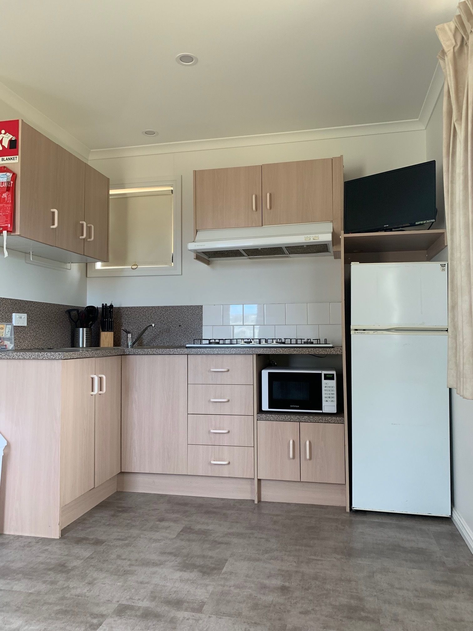 A compact kitchen with light wood cabinets, a microwave, a built-in oven, and a small countertop.