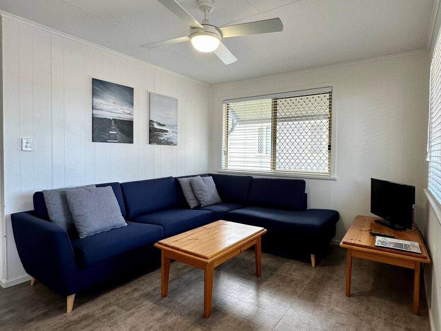 A room with a blue sofa, a wooden coffee table, a TV on a wooden stand, and a ceiling fan.