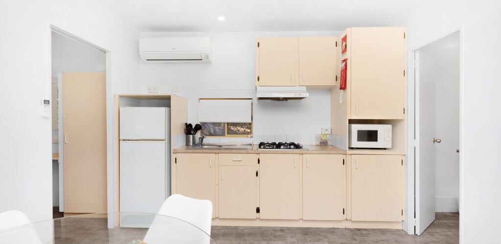 A compact kitchen with beige cabinets, a white refrigerator, a microwave, and a gas stove.