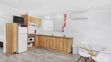 A modern kitchen with wooden cabinets, a built-in oven, a refrigerator, and a glass dining table with chairs.