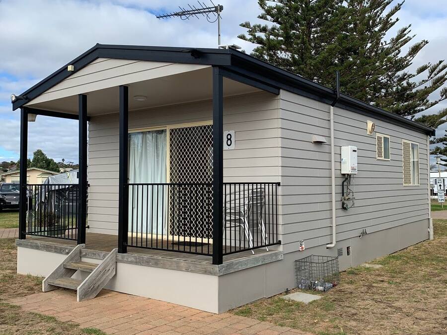 A single-story mobile home with a covered porch, a fenced patio, and a number '8' sign.