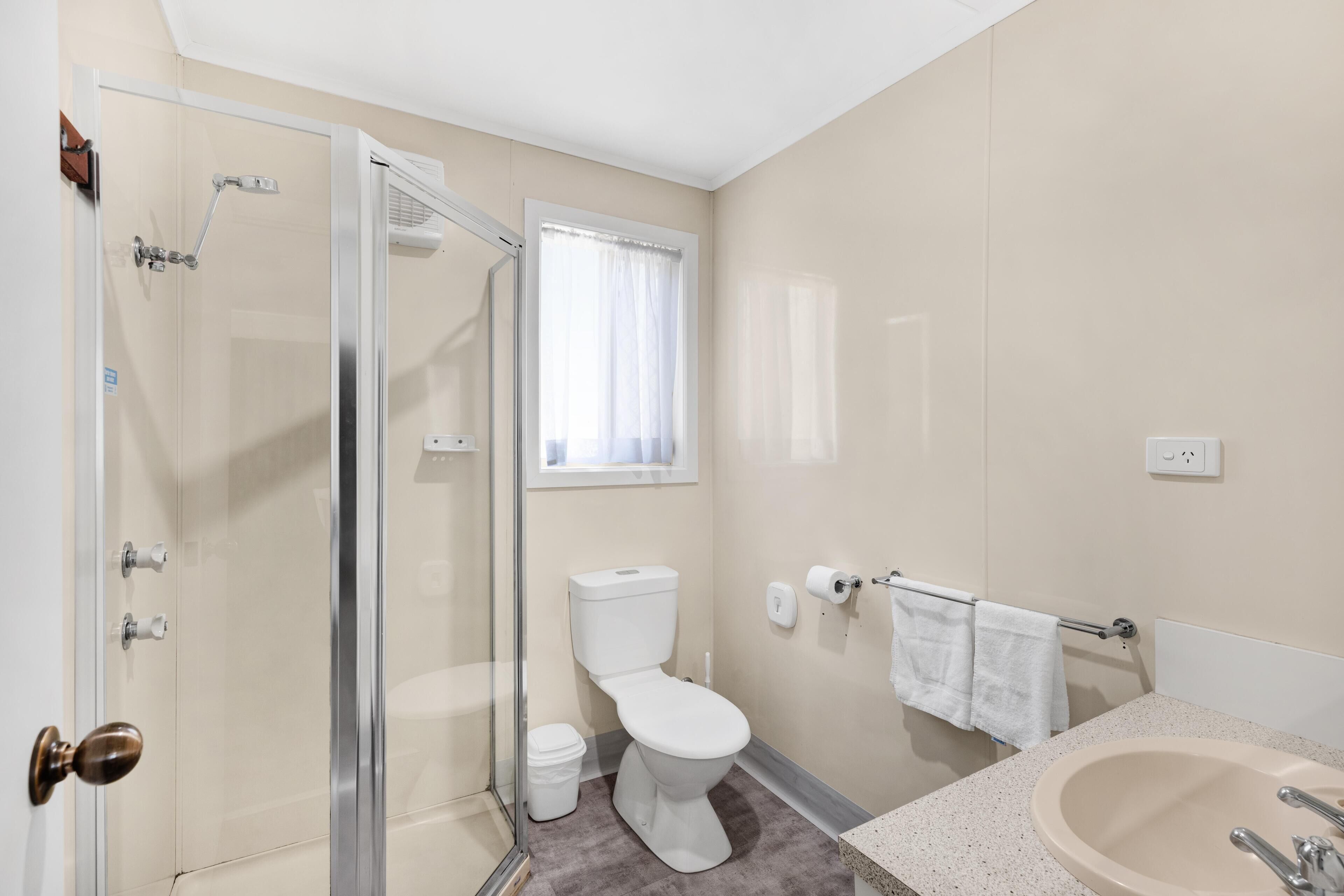 Une salle de bain avec une douche à parois de verre, des toilettes, un lavabo et une fenêtre avec des rideaux.