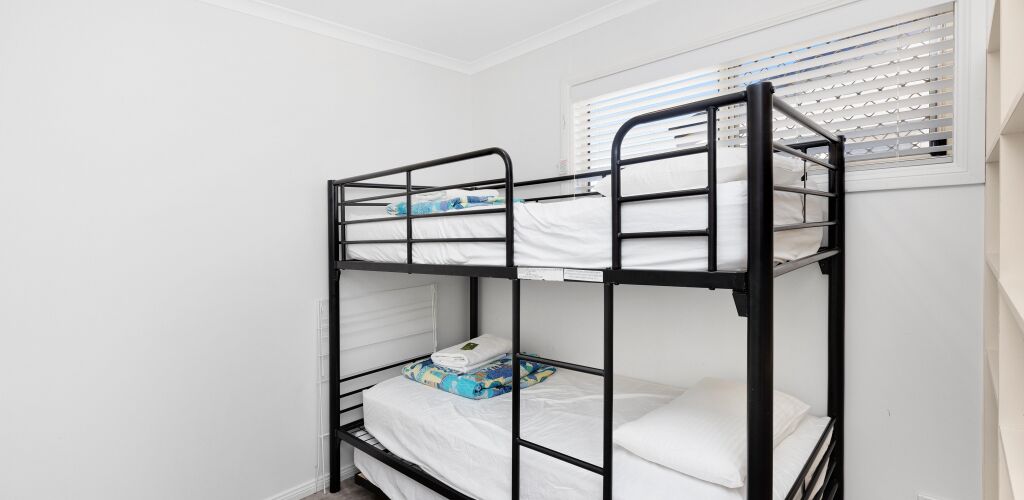 Una cama litera con ropa de cama blanca y una pequeña caja en la cama inferior.