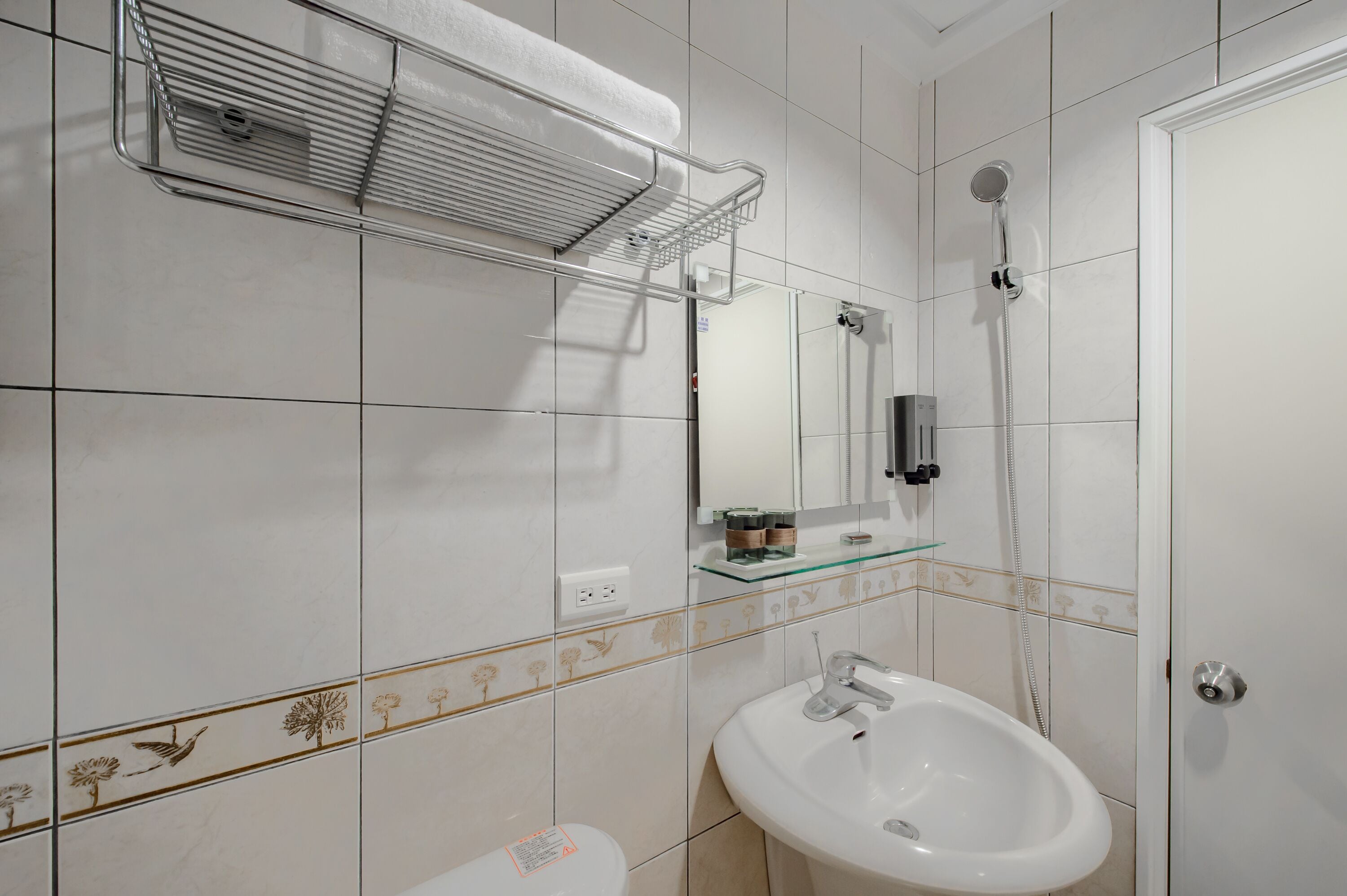 A bathroom with a white sink, a glass shelf, a towel rack, a shower, and a toilet.