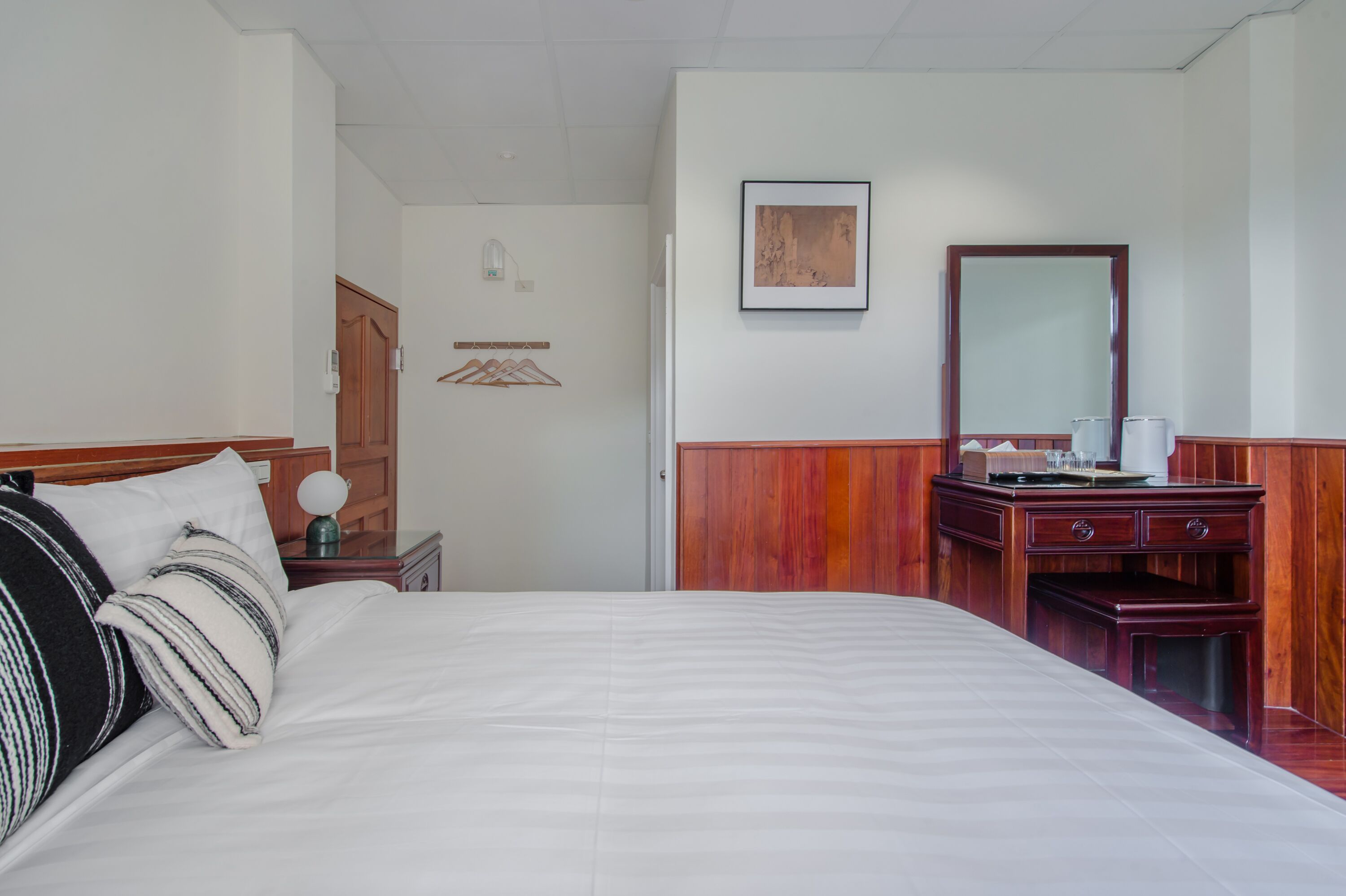A hotel room with a large bed, a wooden dresser, a mirror, and a framed picture on the wall.