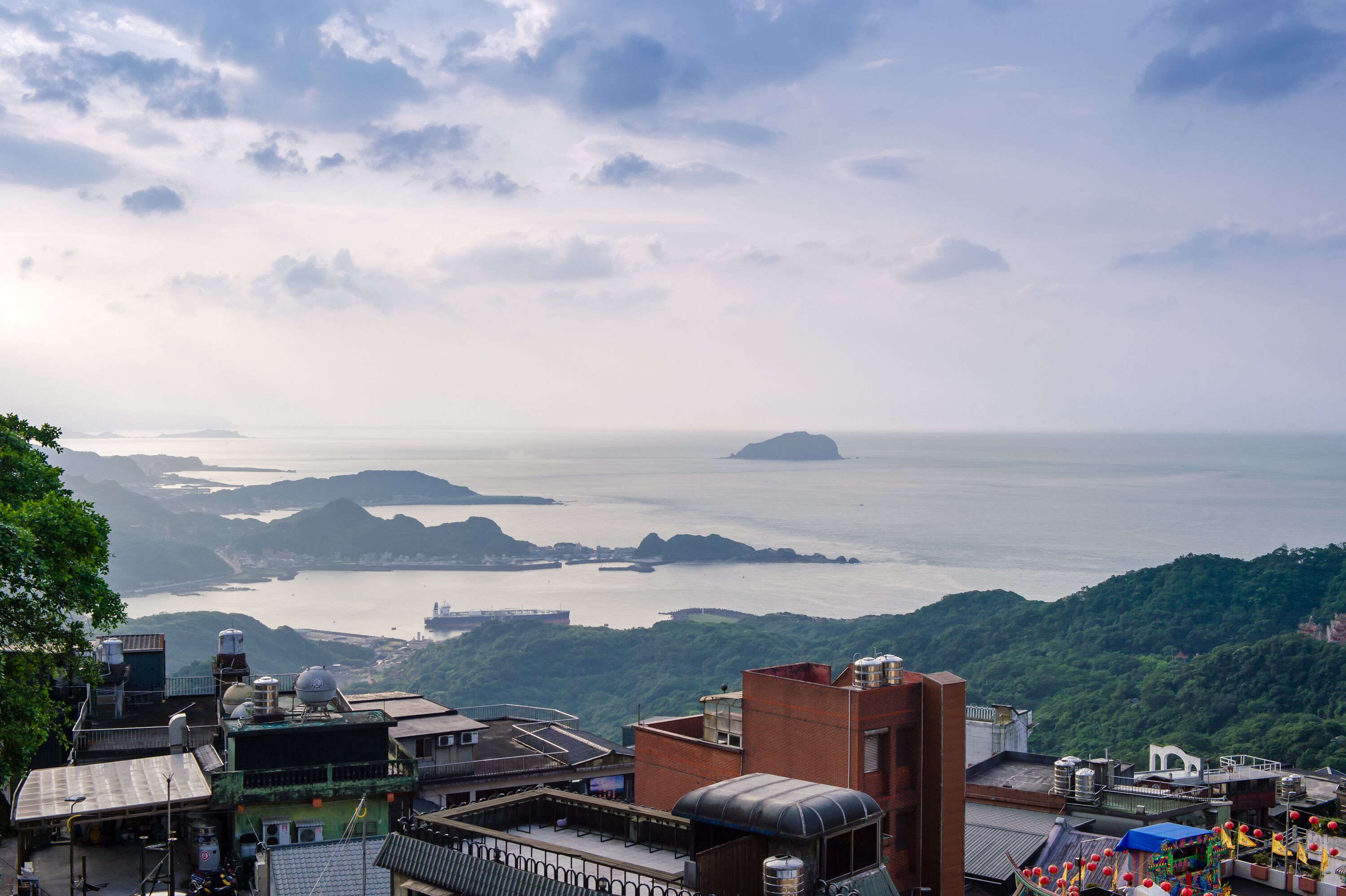 A panoramic view of a coastal city with buildings, a bay, and a distant island.