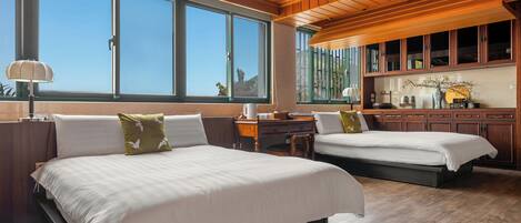 A bedroom with two beds, wooden ceiling, large windows, and a desk with a lamp.