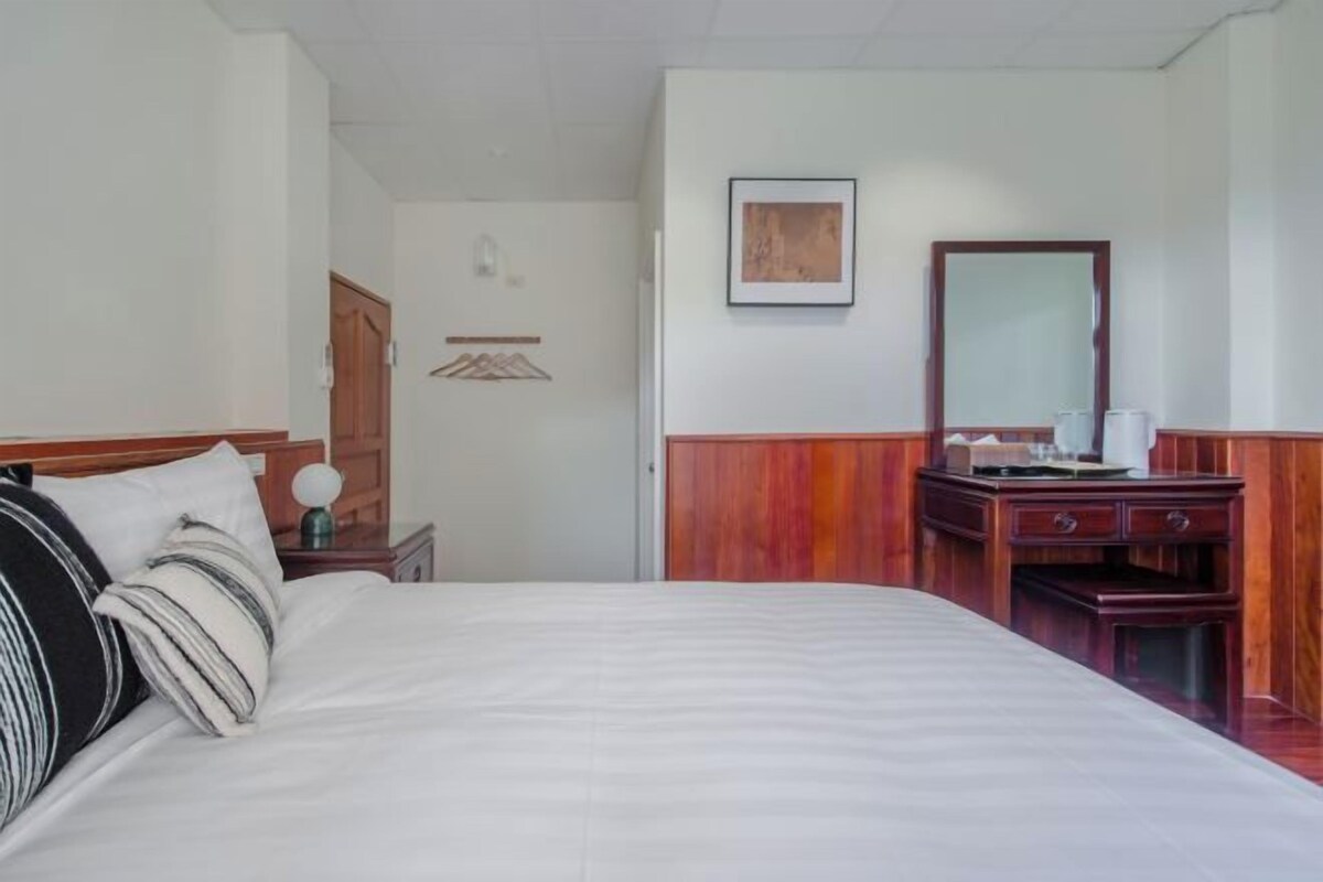 A hotel room with a bed, a wooden dresser, a mirror, and a framed picture on the wall.