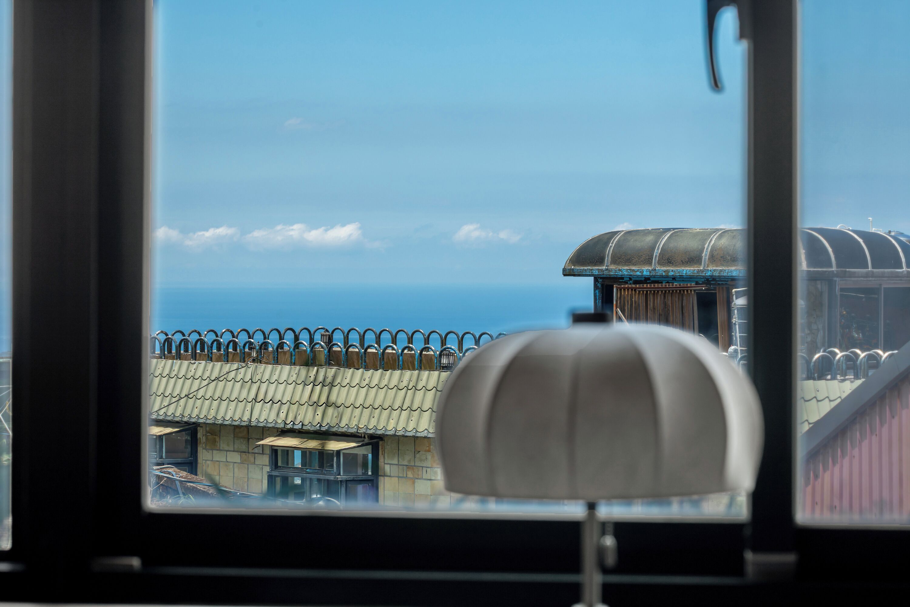 A view from inside a building, looking out through a window at a building with a tiled roof and a fence.