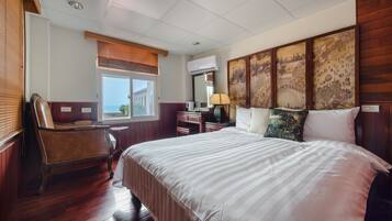Habitación de hotel con una cama grande, una silla de madera, un escritorio con lámpara y una ventana con persianas.