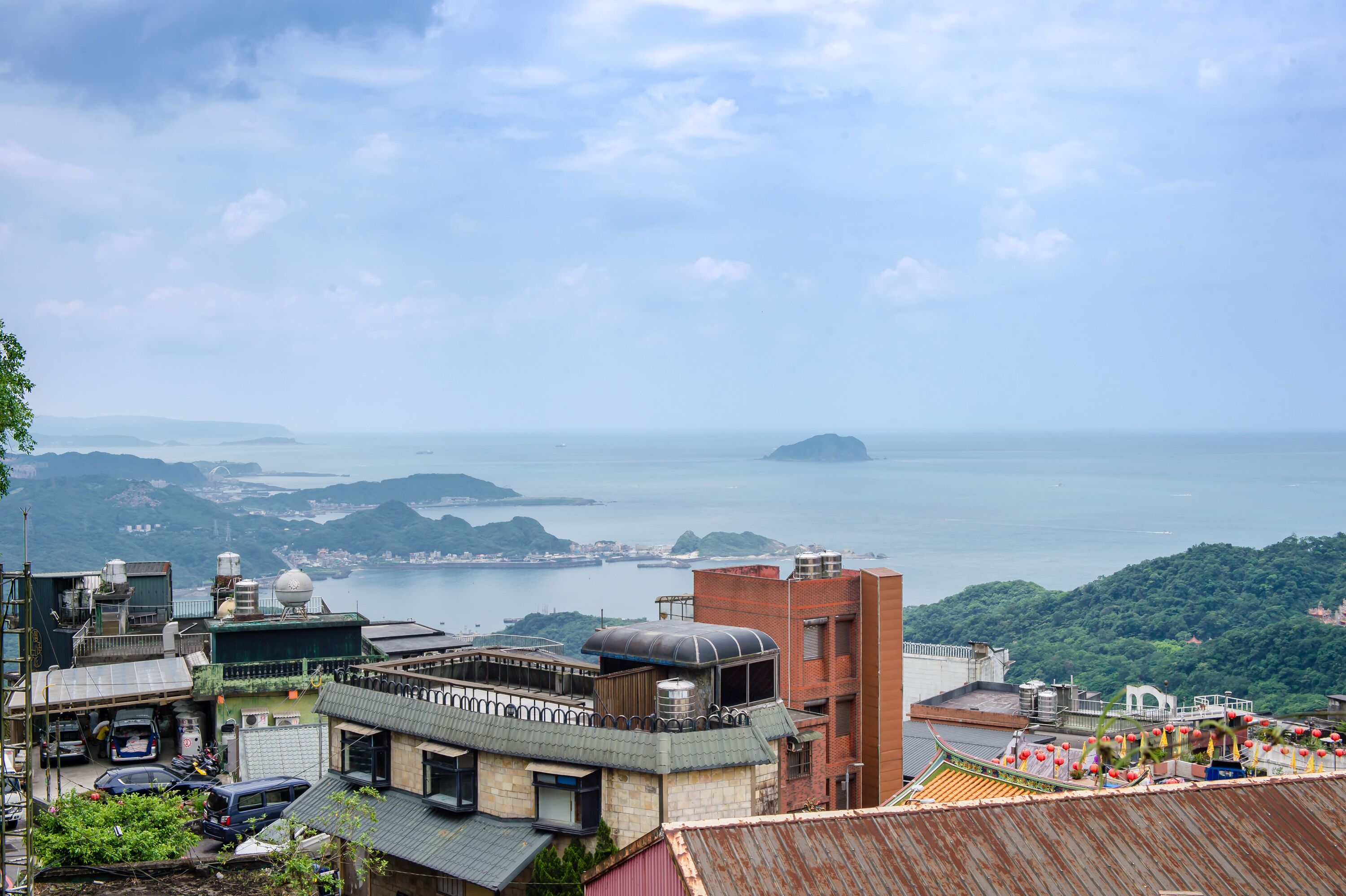 A coastal cityscape with buildings, a view of the sea, and distant islands.