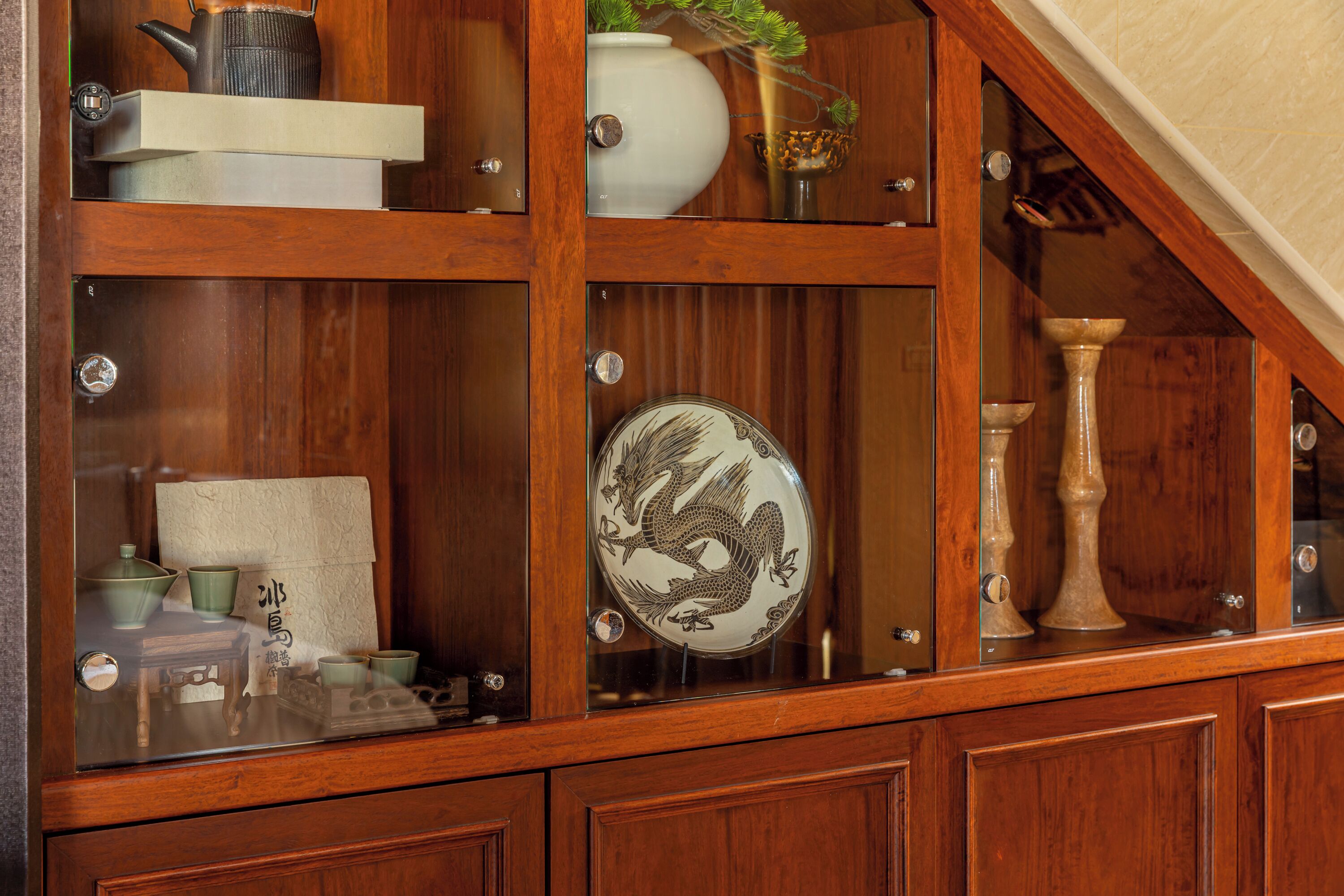 A wooden cabinet with glass doors containing various items like a teapot, a vase, and a decorative plate.