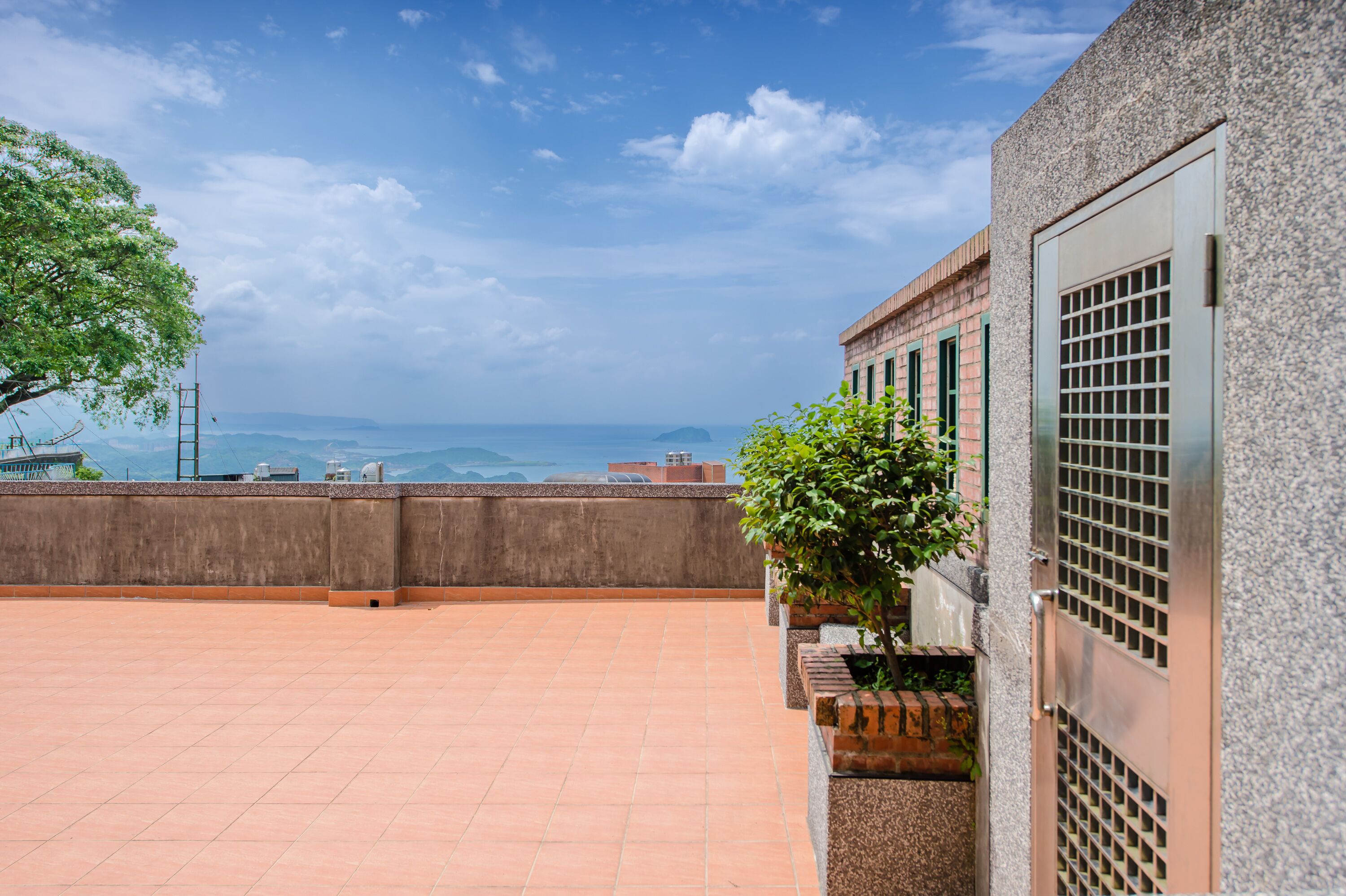 A rooftop terrace with a view of the sea, a concrete wall, and a metal gate.