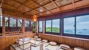 A traditional Japanese-style room with tatami flooring, wooden furniture, and large windows offering a view of the sea. - Jiufen The Dragon Easy Stay (New Taipei City)