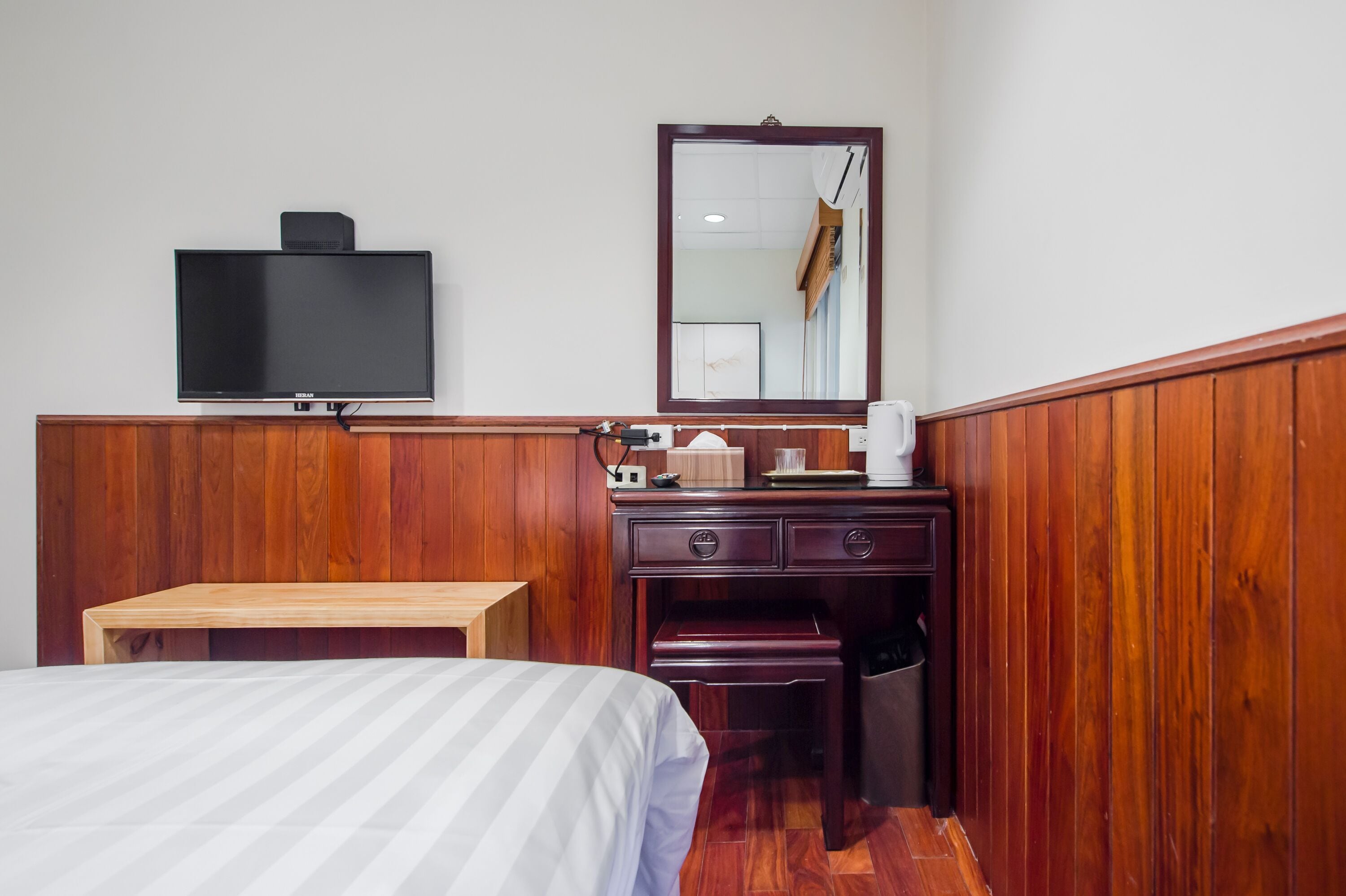 A hotel room with a bed, a wooden desk, a television, a mirror, and a wardrobe.