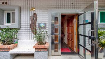 A hotel entrance with a tiled wall, a bench, potted plants, and a glass door leading inside.