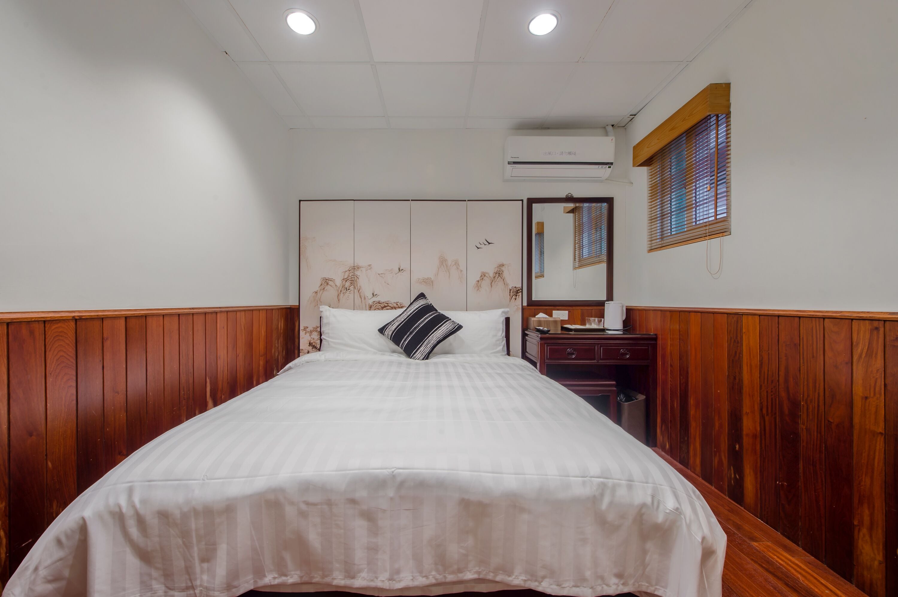A neatly made bed with a striped pillow, a wooden headboard, and a small bedside table with a mirror and a lamp.
