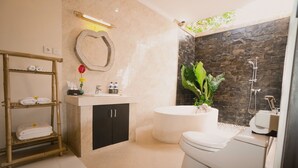 A modern bathroom with a marble vanity, a freestanding bathtub, a toilet, and a bamboo shelf with towels. - Villa Kubu Tanjung Sanur Bali (Denpasar)
