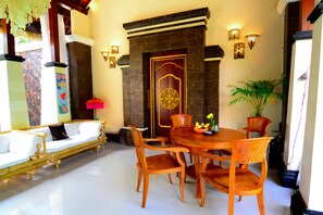 A room with a white sofa, wooden dining table, and chairs, a decorative door, and wall-mounted lights. - Villa Kubu Tanjung Sanur Bali (Denpasar)