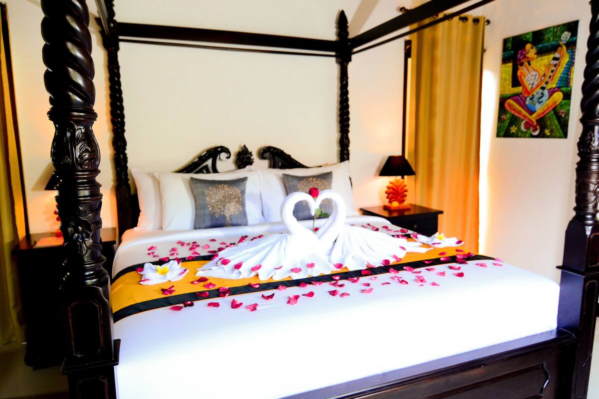 Ein Himmelbett mit herzförmigem Mittelstück, weißer Bettwäsche und Rosenblättern.