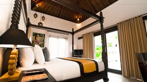 A four-poster bed with a white and yellow bedspread, a black headboard, and a wooden bedside table with a lamp. - Villa Kubu Tanjung Sanur Bali (Denpasar)