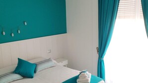 Ein Hotelzimmer mit einem großen Bett, blaustichigen Vorhängen und einem weißen Kopfteil.