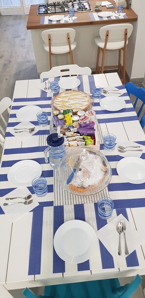 A dining table set with blue and white striped tablecloths, white plates, blue glasses, and a variety of food items including a pie. - Zonaporto (Naples)