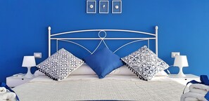 A bed with a white metal frame, blue and patterned pillows, and a white blanket. There are two bedside tables with lamps and a wall with three framed pictures. - Zonaporto (Naples)