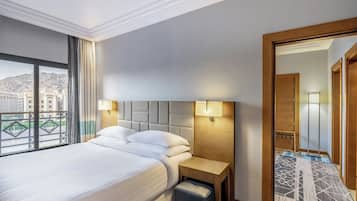 Una habitación de hotel con una cama grande, dos lámparas de noche, una mesita de noche de madera y vistas a la ciudad a través de un ventanal amplio.