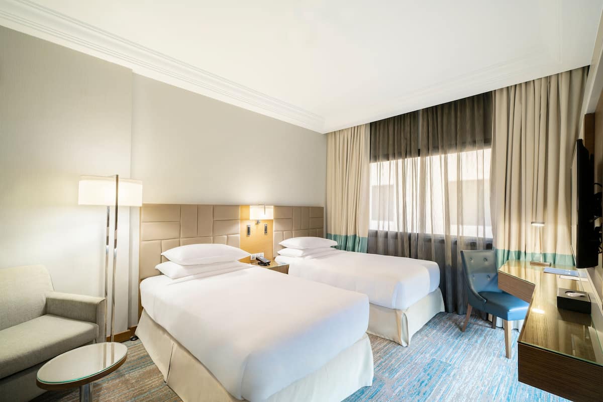 Habitación de hotel con dos camas, un escritorio, una silla, una lámpara y un televisor.