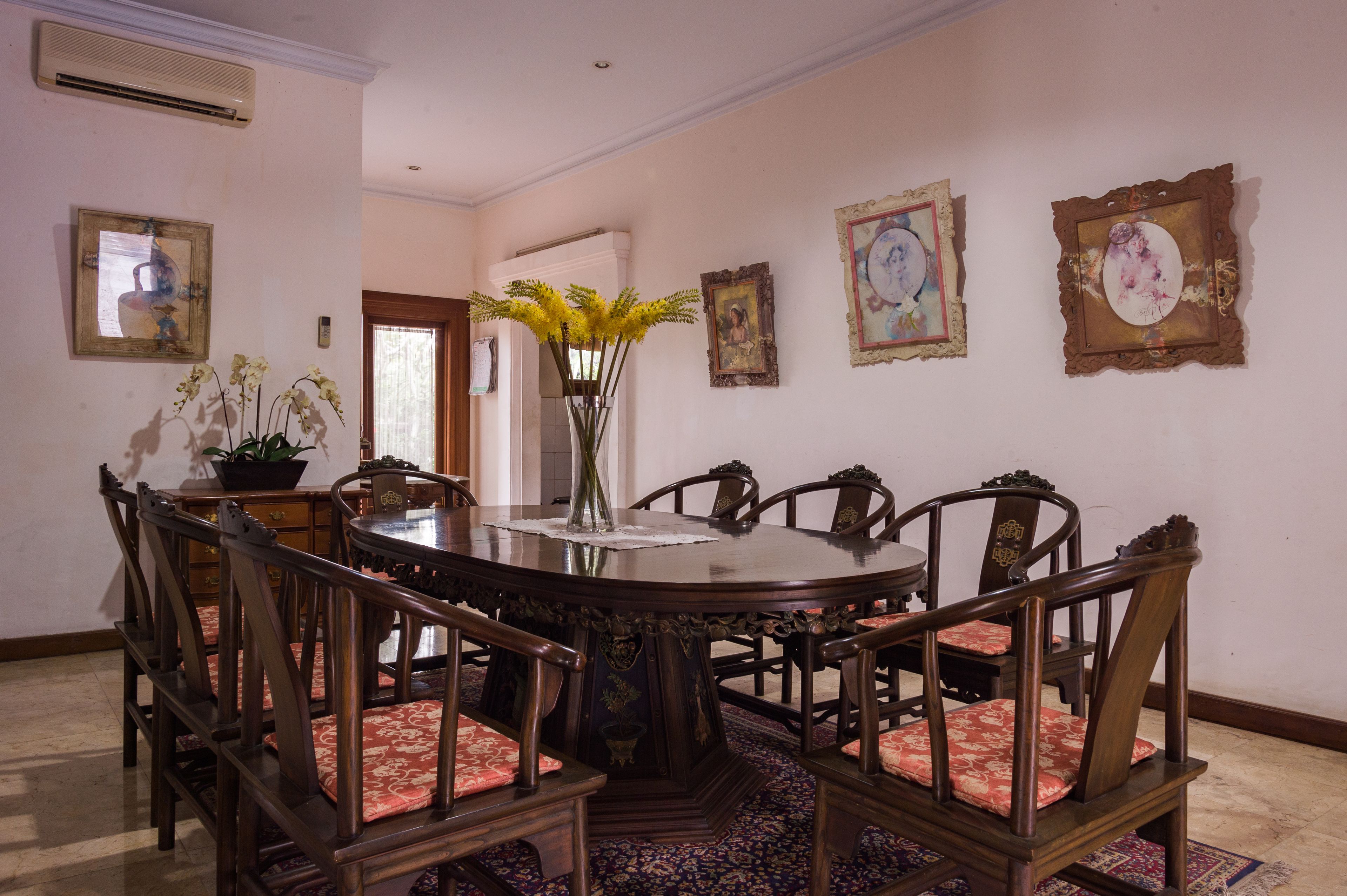 A formal dining room with a round table, six chairs, and a vase with yellow flowers.