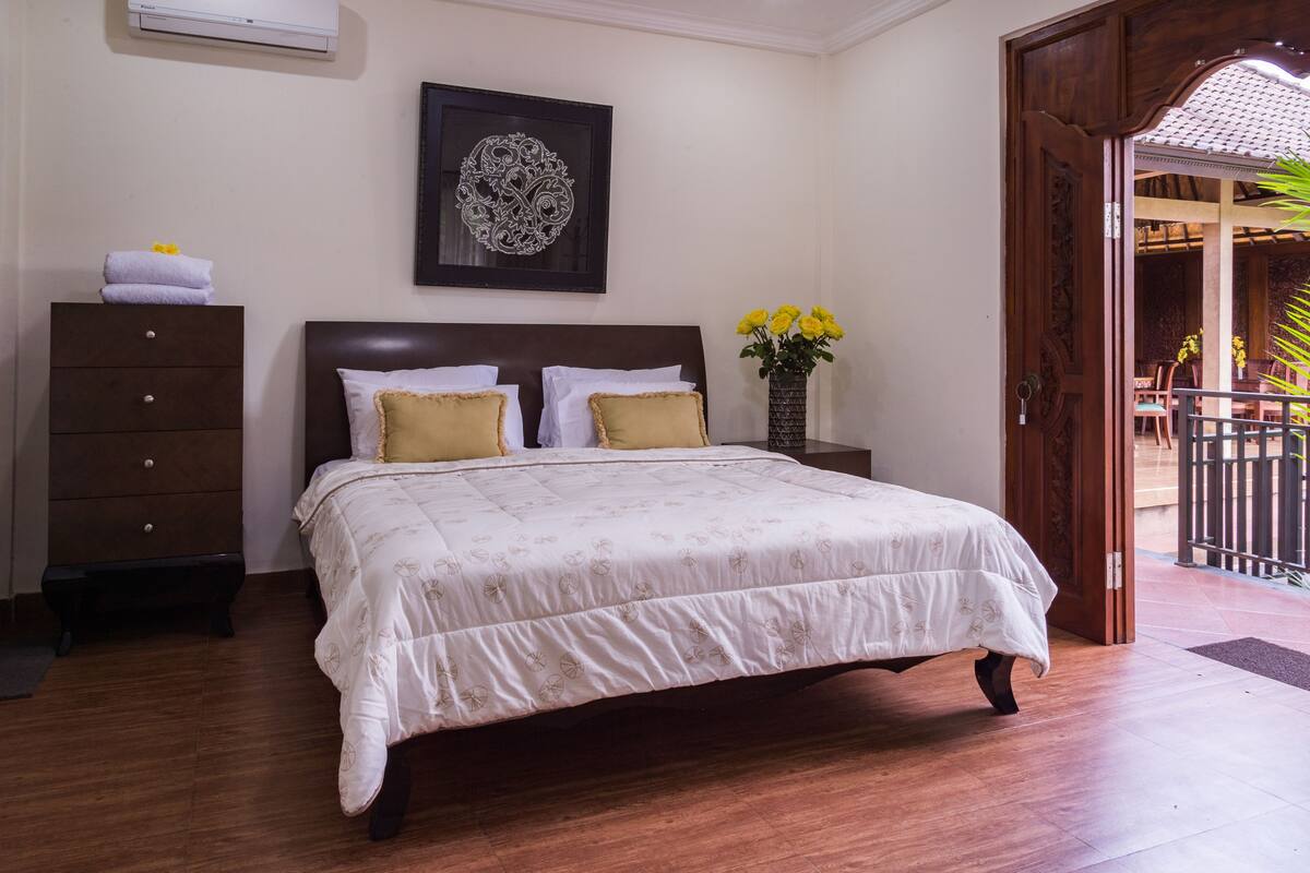 A neatly made bed with a patterned bedspread, a dark wooden headboard, and a wall-mounted decorative piece.
