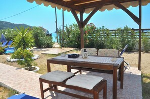Un espace extérieur aménagé avec des meubles en bois, comprenant une table et des bancs, entouré de plantes en pot et offrant une vue sur la mer.