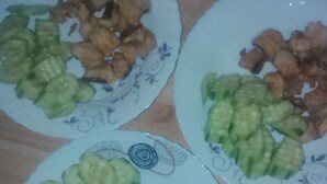 Tres plats d'aliments amb cogombre i aliments fregits damunt un taula de fusta.
