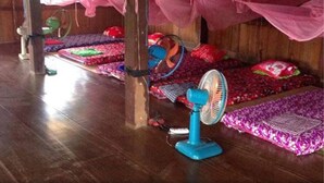 Habitació amb parets de fusta, un llit amb cortina rosa, un ventilador blau i un calefactor verd.