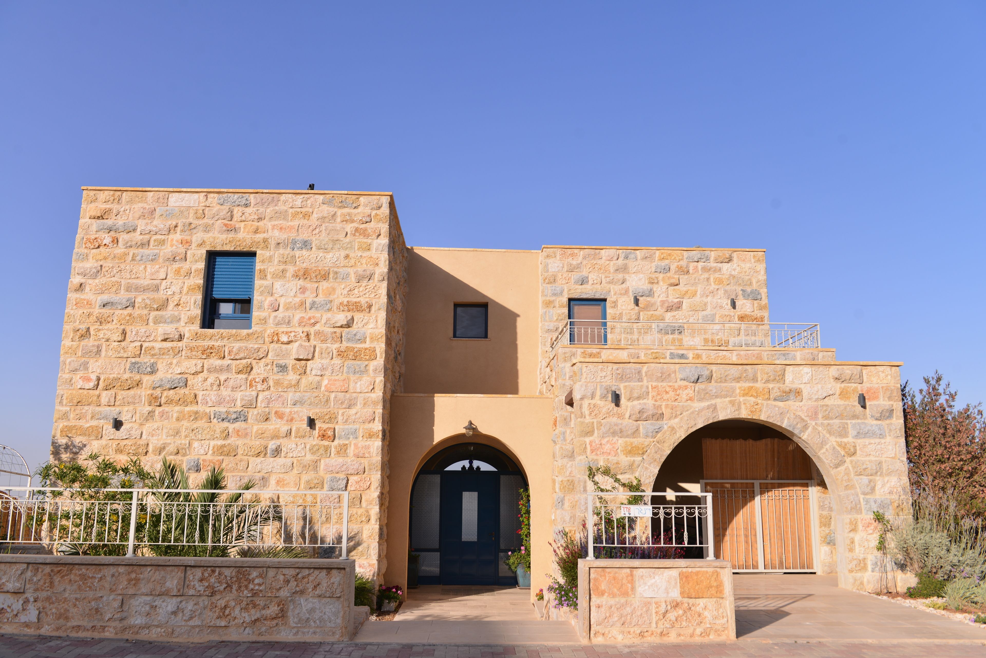 A stone building with a central arched entrance, a small balcony on the upper level, and a gated driveway.