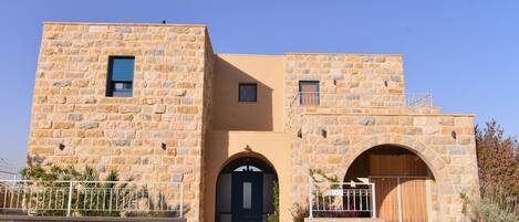 A stone building with a central arched entrance, a small balcony on the upper level, and a gated driveway.