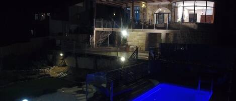 Ein zweigeschossiges Gebäude mit Poolanlage bei Nacht.
