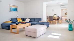 A modern living room with a blue sofa, a wooden coffee table, and a light-colored ottoman. There is a dining area with a wooden table and chairs, and a kitchen visible in the background. - Stunning private villa for 8 people with WIFI, A/C, private pool, TV and terrace (Pazin)