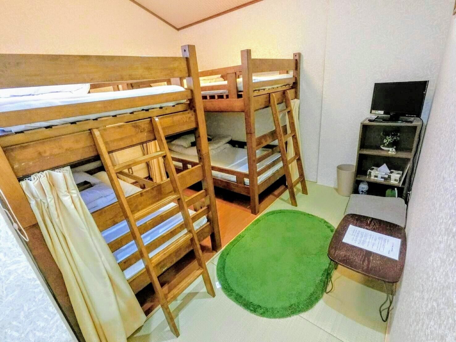 A bunk bed room with a green rug, a small table with a sign, and a shelf with items.